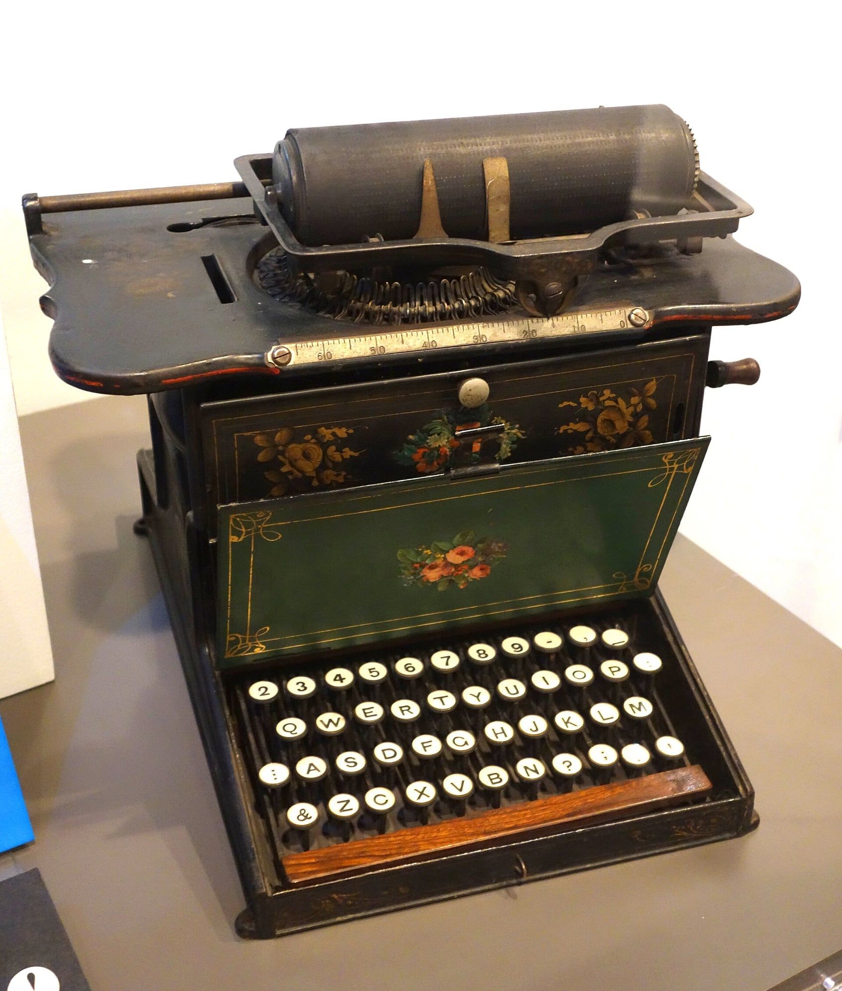 Una máquina de escribir negra del siglo XIX con decoración floral y un teclado de teclas redondas.